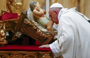 Pope Francis kisses a statue of baby Jesus as he leads the Christmas night Mass in Saint Peter's Basilica at the Vatican